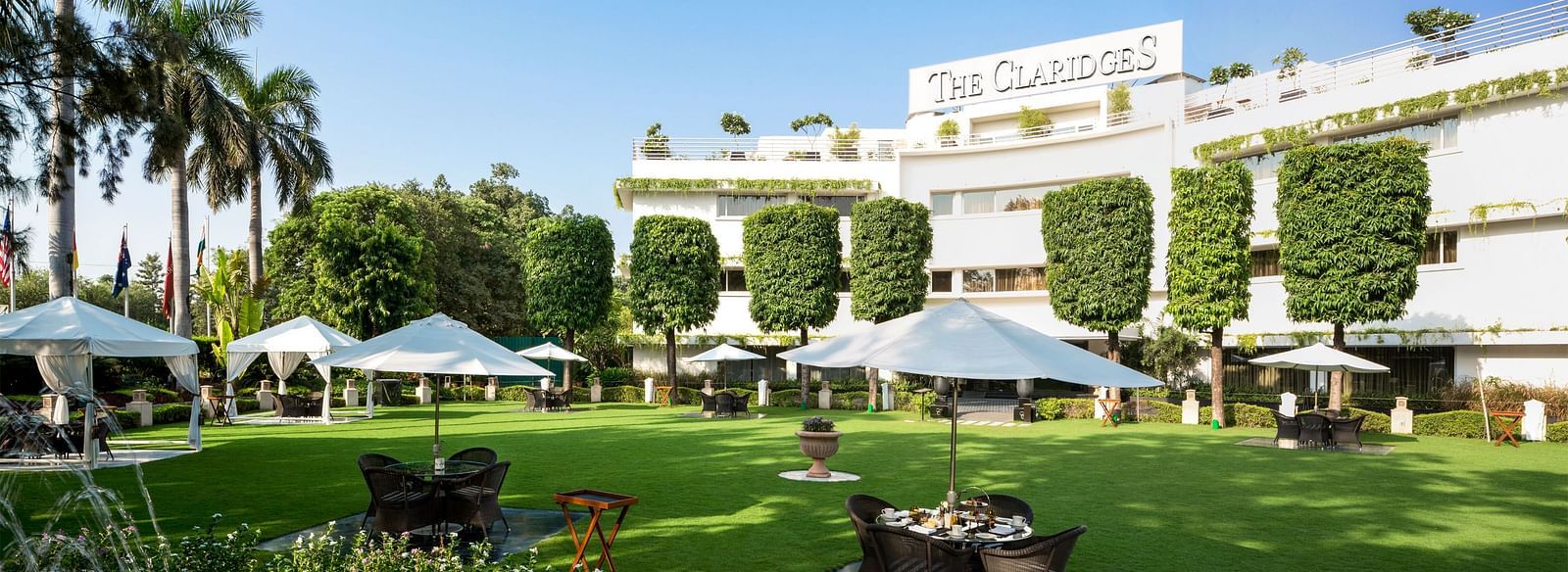 a beautiful landscape image of the claridges garden with glass top coffee tables scattered everywhere - The Claridges New Delhi