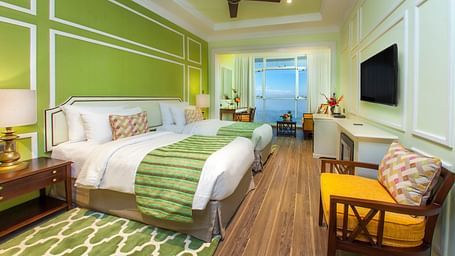  Spacious bed with furniture for seating, a bedside table, and a wall-mounted television at Fragrant Nature Munnar.