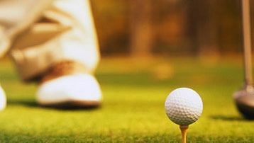 a golf ball on a tee with a persons leg in the background at a golf course - Caravela Beach resort