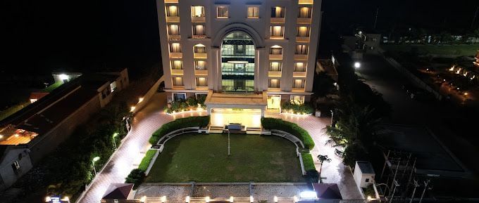 The exterior of a hotel building illuminated at night with a paved pathway and garden | Daksh The Madhuvan Suites