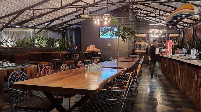  Indoor restaurant space with long wooden tables and chairs, under an exposed ceiling with hanging lights | Astra Hotels and Suites Kadubeesanahalli