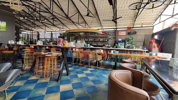 Spacious indoor restaurant with high ceilings, exposed beams, colorful chairs, and a checkered blue and white floor | Astra Hotels and Suites Kadubeesanahalli