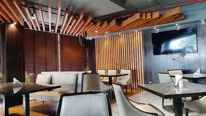 A restaurant with modern tables for four, wooden decorations towards the wall and ceiling, along with a wall-mounted TV at Yashshree The Imperial Inn, Siliguri.
