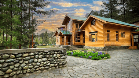 An exterior view of a multi-storey wooden cottage building with a paved courtyard area and a stone wall under a sunset sky.