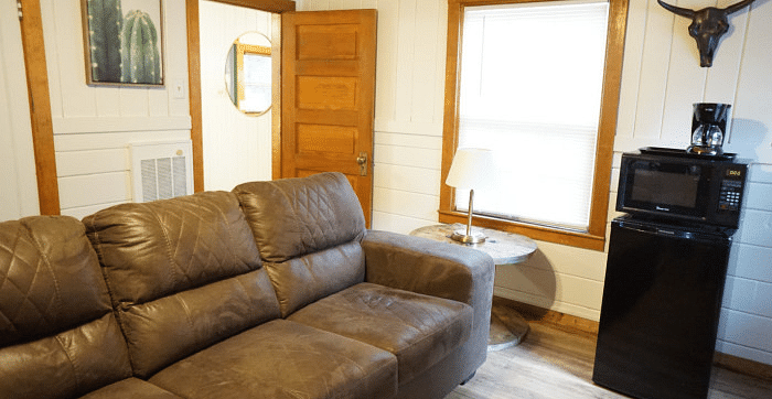 Overview of a Room at Shaver Lake Village Hotel with a brown leather couch, mini fridge, microwave, window, and a bull skull decoration on the wall.