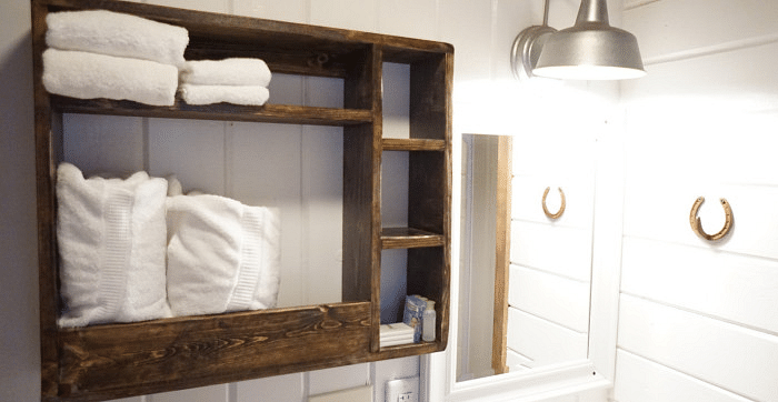 Overview of a Bathroom at Shaver Lake Village Hotel with a wooden shelf holding white towels, horseshoe decorations, and a silver light fixture.