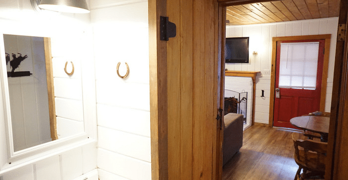 Overview of a bathroom at Shaver Lake Village Hotel, through a wooden doorway, showing a living area with a fireplace and red door.