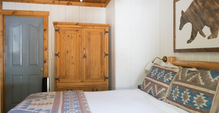 Overview of a Room at Shaver Lake Village Hotel with a wooden armoire, patterned pillows on a bed, a bear silhouette artwork, and a grey door.