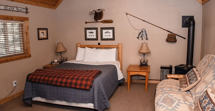 Overview of a Room at Shaver Lake Village Hotel with a bed, plaid blanket, couch, fishing decor, wood ceiling, and a small window.