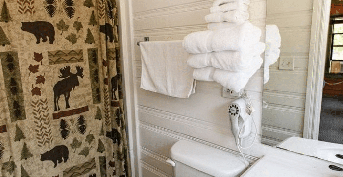 interior of a Bathroom at Shaver Lake Village Hotel with bear and moose themed shower curtain, white towels, and a water closet.