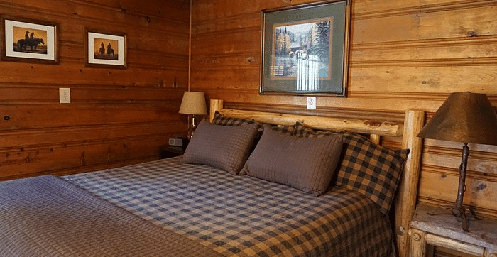 a Bedroom at Shaver Lake Village Hotel with a wooden bed frame, plaid bedding, wood paneled walls, and framed artwork.