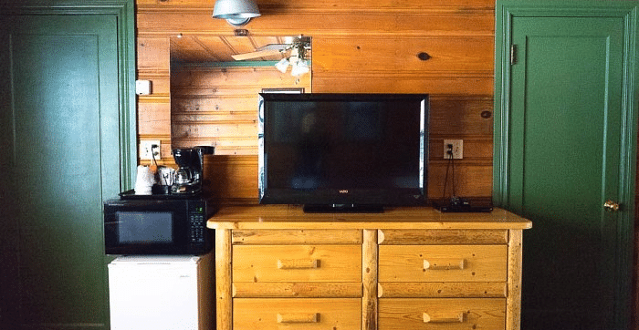 interior of a Room at Shaver Lake Village Hotel with a wooden dresser, TV, microwave, coffee maker, and two green doors against wood paneled walls.
