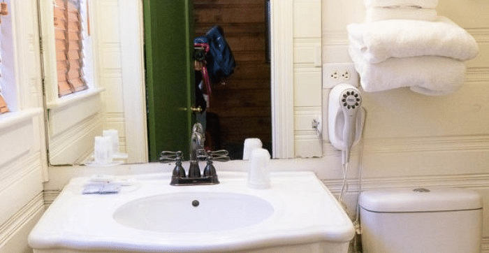 view of the vanity area in a room at Shaver Lake Village Hotel with a white basin, toiletries, a mirror reflecting a doorway, and stacked white towels.