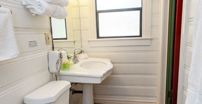 Overview of a Bathroom at Shaver Lake Village Hotel with white pedestal sink, toilet, stacked towels, and a window with natural light.