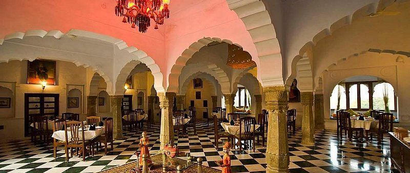 An elegant dining hall at Fort Barli, with arched ceilings, checkered floors, and a vibrant chandelier, blends historical architecture with a refined dining experience.