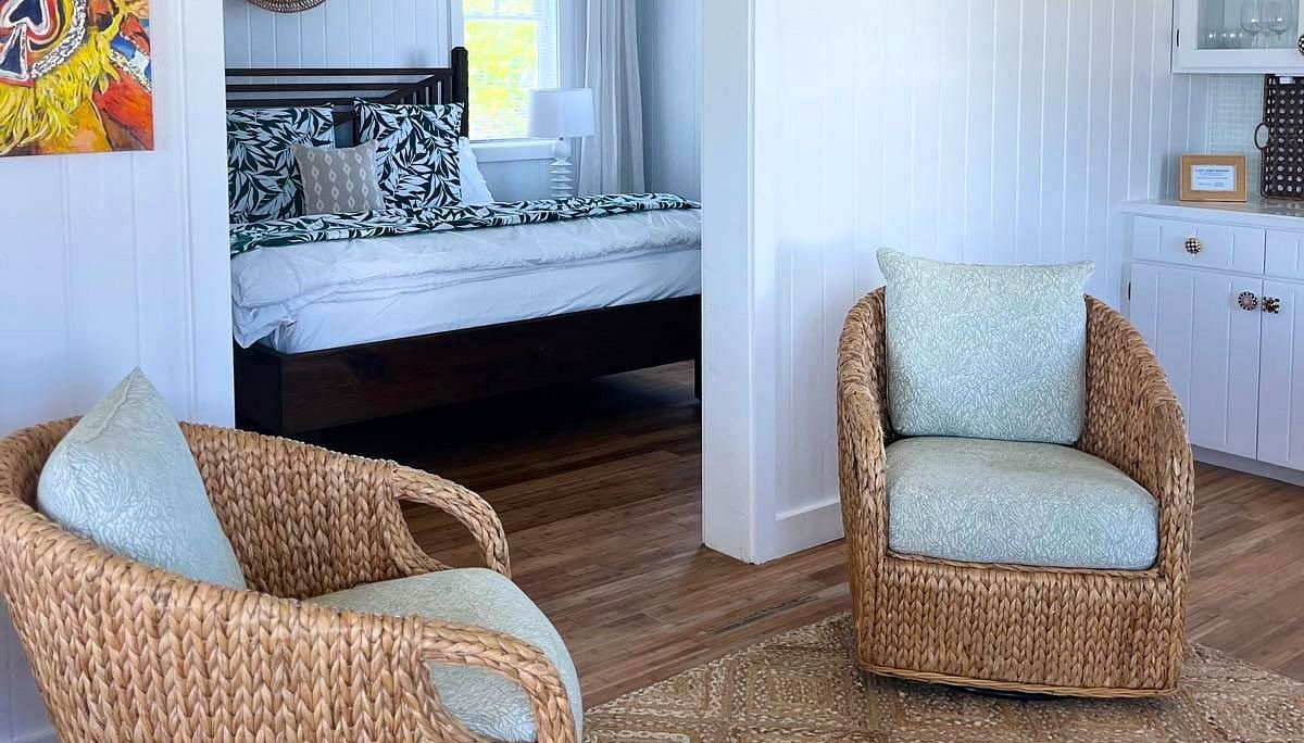 An interior view of a room with tiled floors. Two wicker chairs and a small table are in the foreground, with a glimpse into another room with a mirror and artwork on the wall | Abaco Inn