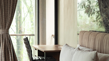 A sunlit bedroom with a desk by a glass door that opens to a lush green forest at Stanley Revelation.