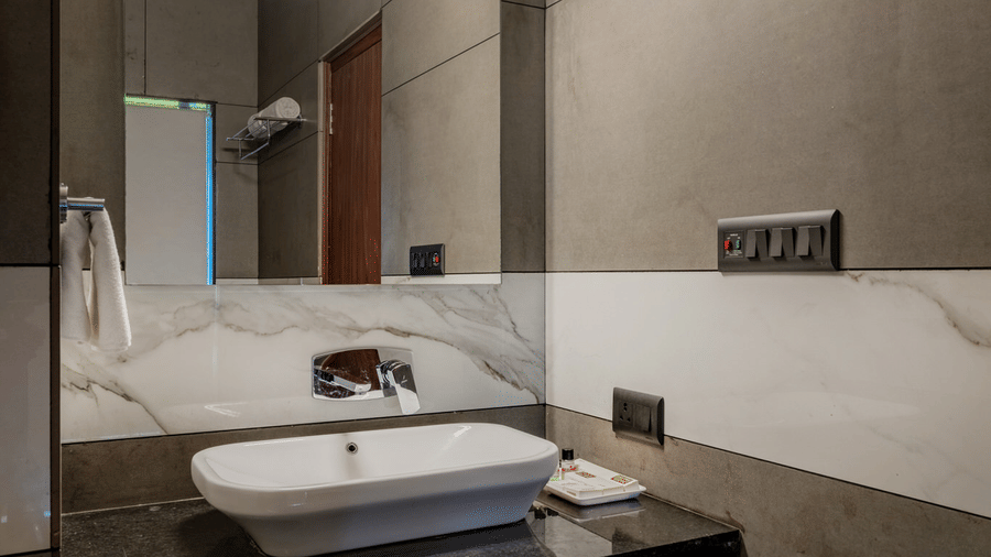 A modern bathroom featuring a vessel sink on a dark countertop below a rectangular mirror with lighting.