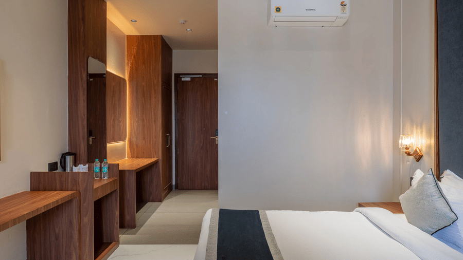 Plush double bed & the wall-lit hallway with cabinets and wardrobe in the Super Deluxe Room at Hotel Highway Prince, Behror.