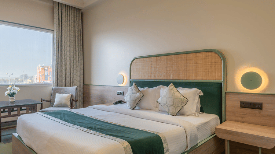 A wide view of a Hotel Highway Prince, Behror bedroom featuring a double bed with green accents, a ceiling fan, and a window with curtains.