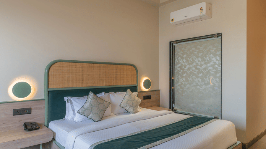  A guest room at Hotel Highway Prince, Behror, featuring a queen-sized bed with white linens, a teal runner, and a wooden curved headboard.