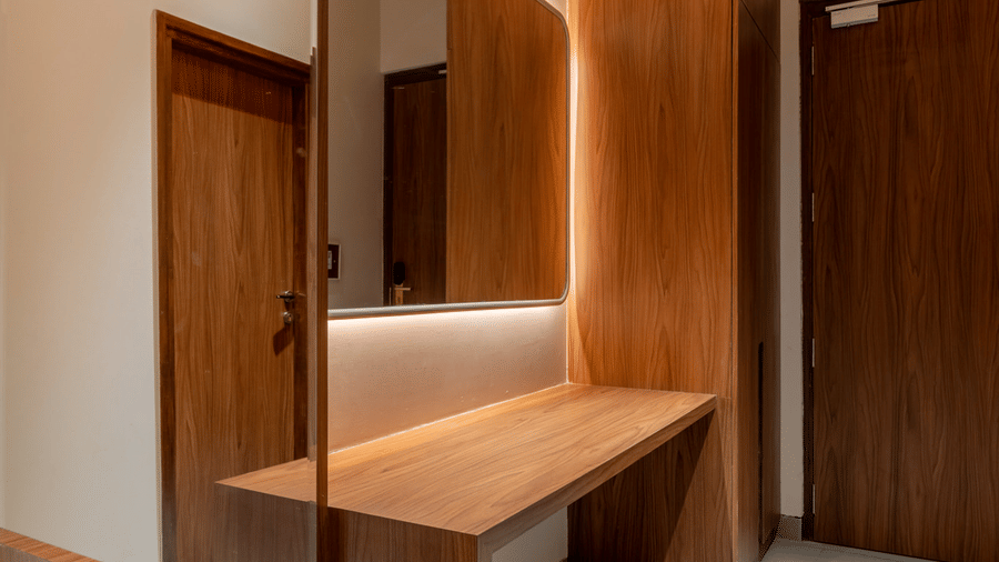 Modern vanity area at Hotel Highway Prince, Behror, featuring a long wooden desk, a vertical wall mirror, and wood-paneled doorways.
