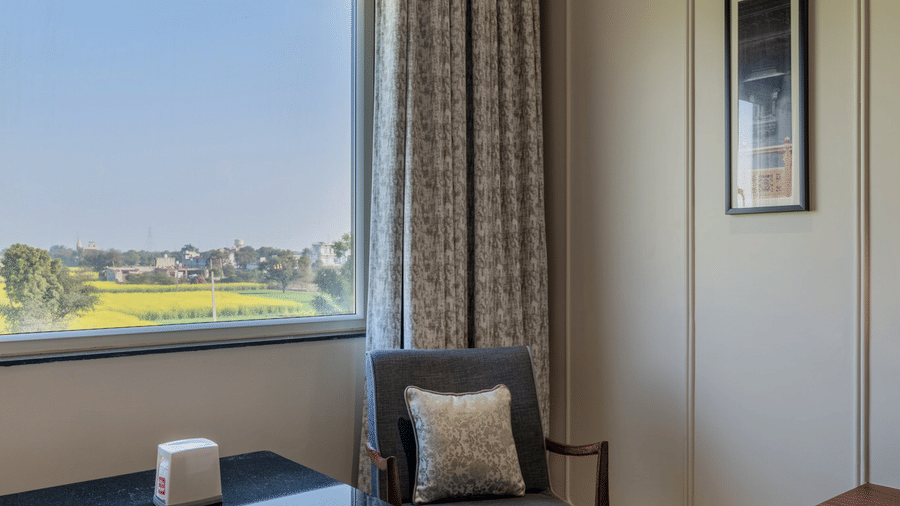 Seating area in a room at Hotel Highway Prince, Behror, with two armchairs, a small table, and a large window overlooking the outdoors.