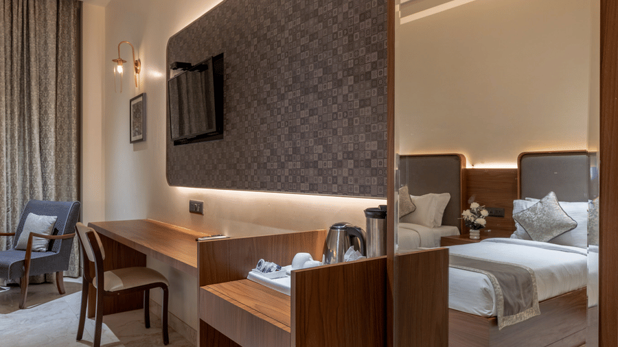 A narrow view of a room hallway with a wooden dressing table, a large mirror, and a seating area in the distance.