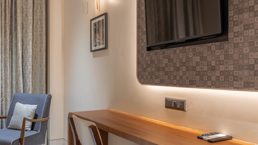 A long wooden built-in desk with a chair and a wall-mounted flat-screen television in a well-lit room at Hotel Highway Prince, Behror.