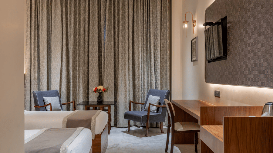 Twin bedroom at Hotel Highway Prince, Behror with two single beds, dark wood accents, and a large window with floor-to-length curtains.