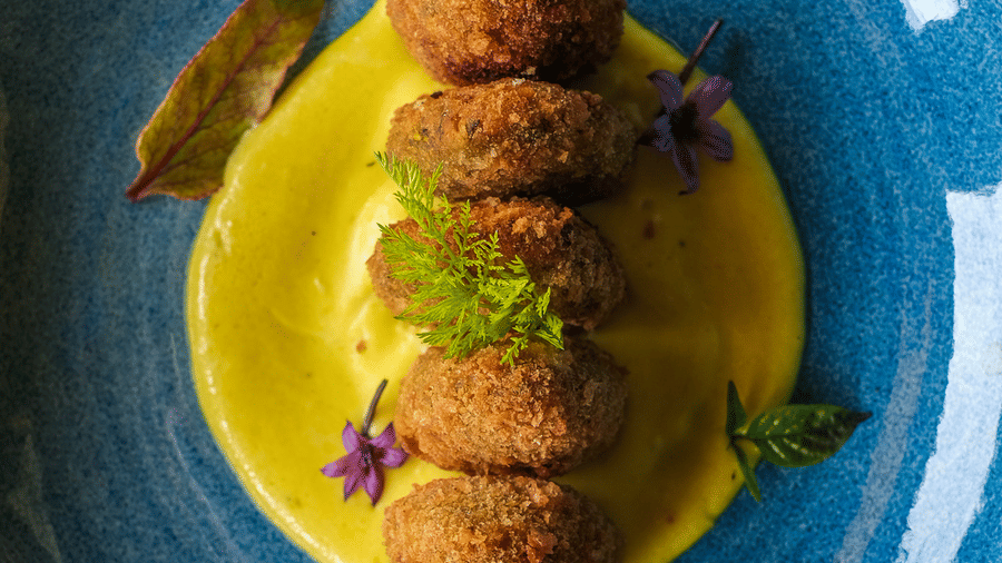 Vegetable croquettes served on a bed of yellow puree in a blue ceramic bowl at Rhino & River Wildlife Retreat & Spa, Pobitora