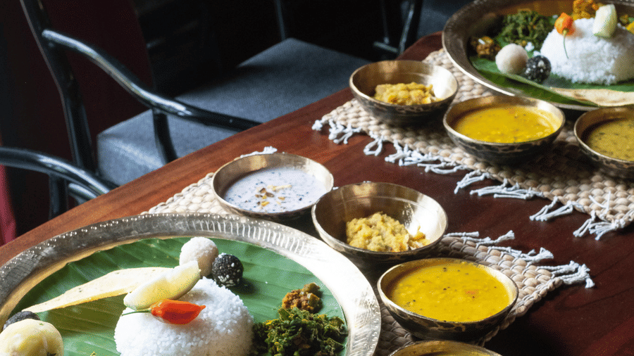 traditional Assamese Thali meal featuring rice and multiple small bowls of curries on a wooden table at Rhino & River Wildlife Retreat & Spa, Pobitora.