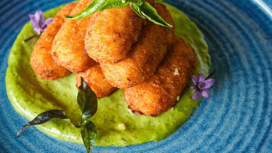 Golden-brown fried croquettes served over a vibrant green puree in a blue textured bowl at Rhino & River Wildlife Retreat & Spa, Pobitora.