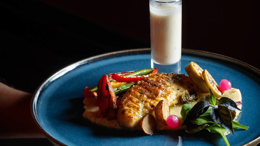 A server holding a blue plate with a gourmet entree and a small glass of white beverage at Rhino & River Wildlife Retreat & Spa, Pobitora