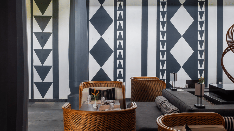 A vertical shot of the lobby at Rhino & River Wildlife Retreat & Spa, Pobitora, featuring woven wicker chairs and walls decorated with bold black-and-white geometric patterns.