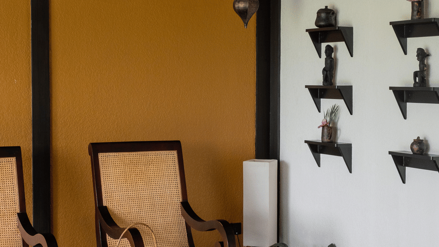 A corner lounge with high-backed wooden chairs and black decorative wall art at Rhino & River Wildlife Retreat & Spa, Pobitora.