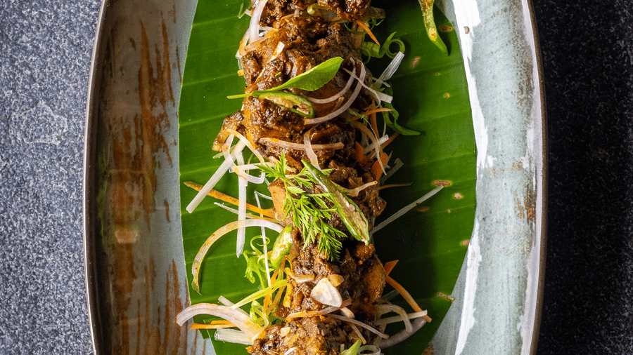 A long oval platter featuring a garnished meat dish served on a banana leaf at Rhino & River Wildlife Retreat & Spa, Pobitora.