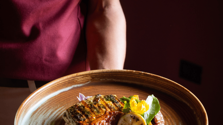 A server in a maroon uniform presenting a beautifully plated entree at Rhino & River Wildlife Retreat & Spa, Pobitora.