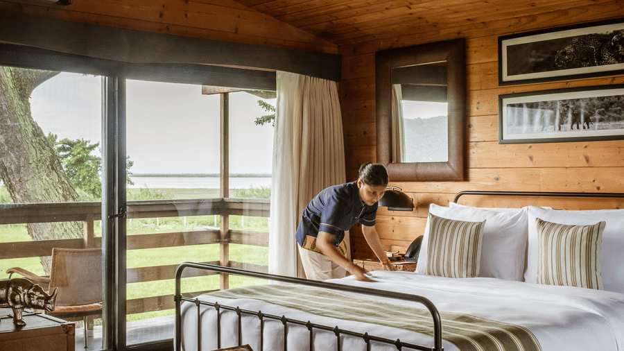 A vertical shot of a guest room at Rhino & River Wildlife Retreat & Spa, Pobitora, showing a bed with a black metal frame and a glass door leading to a balcony.