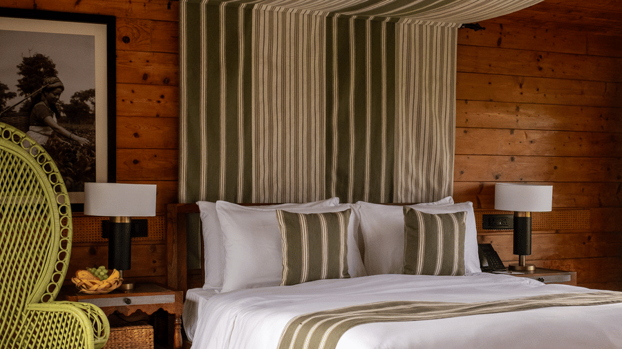 vertical shot of a guest room at Rhino & River Wildlife Retreat & Spa, Pobitora, featuring a large lime-green wicker chair, wooden walls, and a bed with a striped canopy.