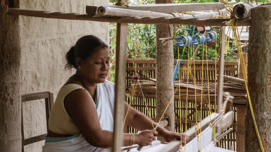 A side profile shot of a local woman working on a large, outdoor handloom at the Rhino & River Wildlife Retreat & Spa, Pobitora.