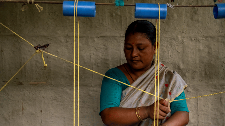 A close-up portrait of a woman’s hands carefully guiding yarn through the intricate threads of a loom