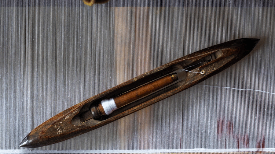 A horizontal view of a classic dark wood shuttle used on a loom, identical to the top-left shuttle.