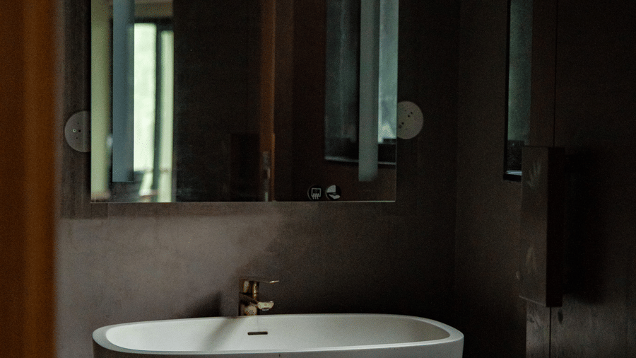 A modern, oval-shaped white sink sits on a marble counter in a dim bathroom at Stanley Revelation.