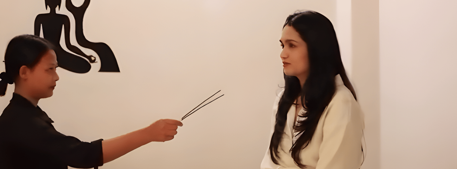 A woman sitting on the spa bed while a spa specialist stands before her holding incense sticks at Bamboo Saa Sunrise Wedding & Wellness Resort, Jaipur.