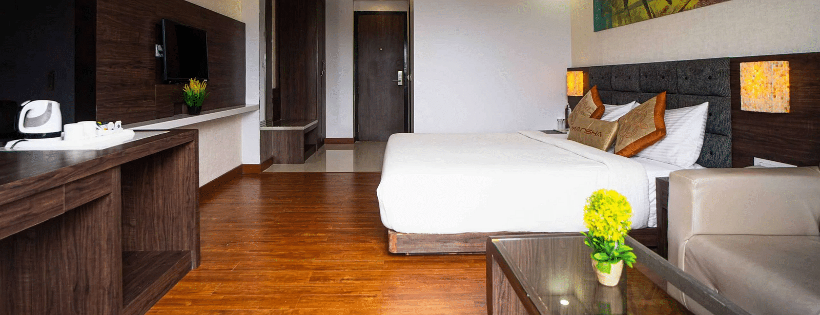 A hotel room at Mansha Hotel Regency with a large bed, wooden flooring, and a ceiling fan.