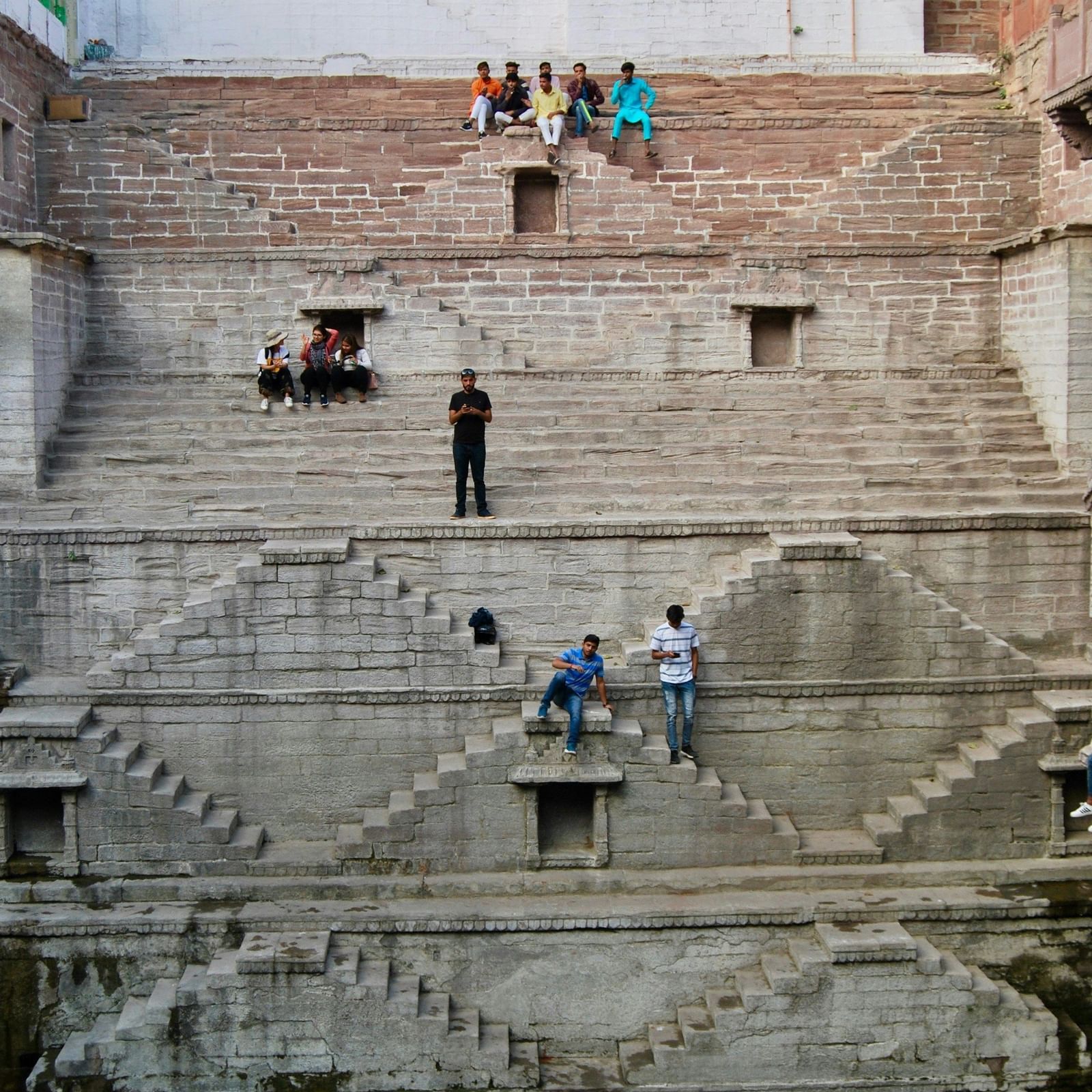 A stepwell with people sitting on the steps and a waterbody below