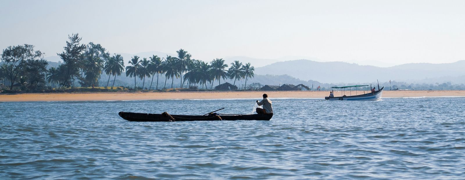a fisherman pulling a fishing net with palolem beach in the background