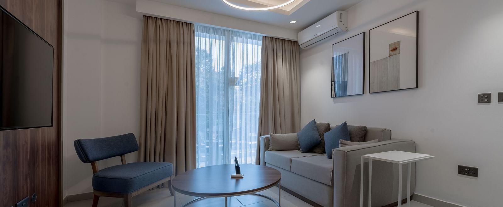 A modern living room in a Premier Suite with stylish furniture, large windows, and elegant decor. - The Pelican Hotel, Accra