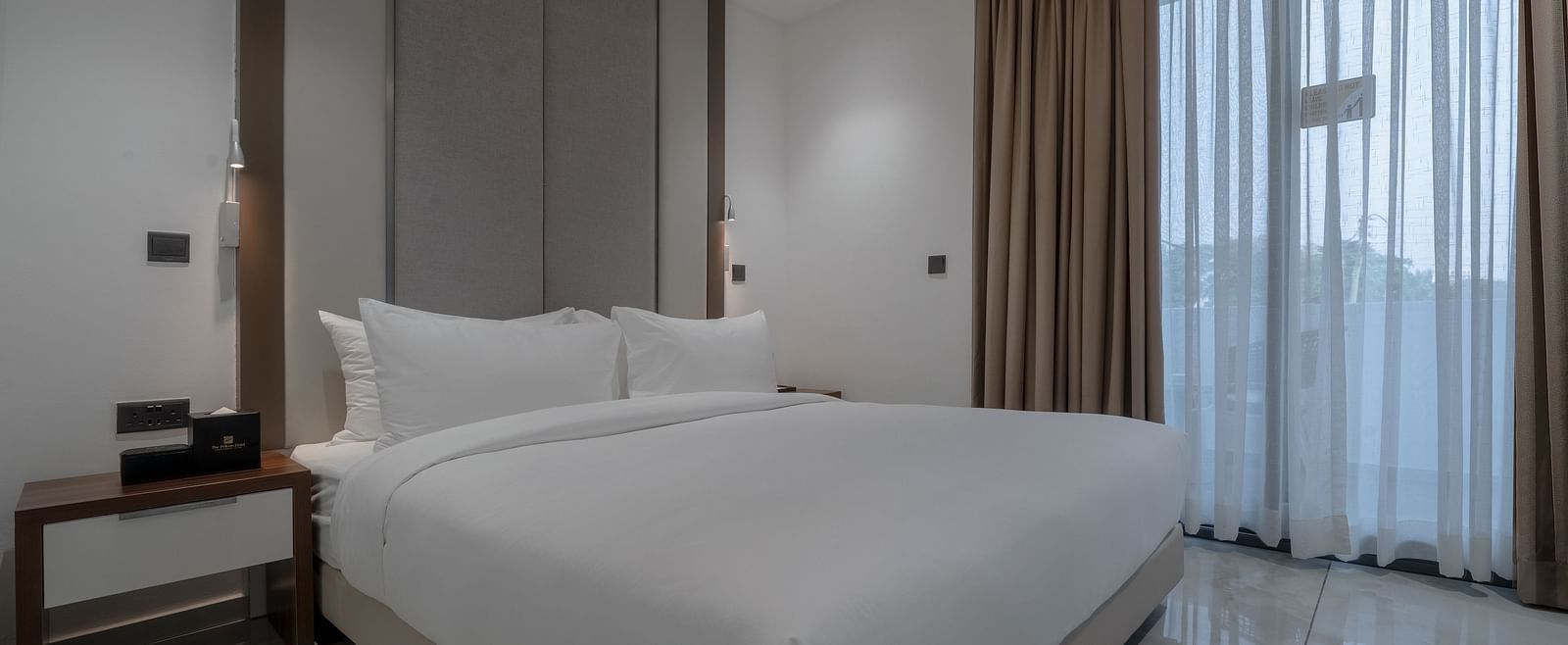 A modern and spacious Deluxe Room with a king size bed, sitting area, and large windows for natural light. - The Pelican Hotel, Accra